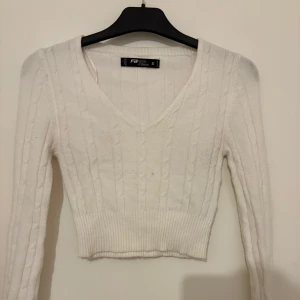 Vit stickad croppad tröja från FB Sister - Säljer en vit stickad croppad tröja från FB Sister. Tröjan har v-ringning, lång ärm och ribbad midja. 