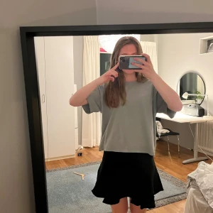 Svart volangkjol - Säljer en svart kortkjol med volangkant. Kjolen har en enkel och stilren design som passar perfekt till många olika outfits. Den är lätt och har en snygg, svängande form nertill.