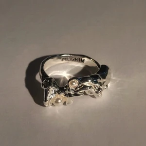 Silver plated ring med pärlor från Pilgrim - OANVÄND ADJUSTABLE Unik silverfärgad ring från Pilgrim med organiskt formad design och små vita pärlor som detaljer. Ringen har en modern och konstnärlig look som sticker ut och passar perfekt för dig som gillar statement-smycken.