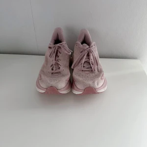 Rosa HOKA Löparskor - Ett par rosa HOKA W CLIFTON 9 löparskor som är flitigt använda men fortfarande i gott/bra skick! Som man ser på bilderna så finns det några tecken på användning så som smuts på yttersulan, på tyget och märkes och storleks lappen är lite avskavd. Jag har tvättat dom men all smuts gick inte bort. Tyvärr så är dom lite för små för mig nu, därav säljs dom. Nypris 2000kr! FÖRST TILL KVARN!