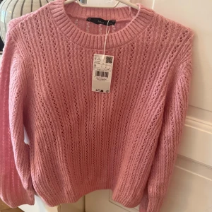 Rosa stickad tröja från MANGO - Superfin rosa stickad tröja från MANGO med hålmönster och rund halsringning. Tröjan har långa ärmar och ribbade muddar vid ärmslut och nederkant. Perfekt för lager-på-lager under kyliga dagar.