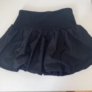 Svart volangkjol från Gina Tricot - Supersöt svart kortkjol från Gina Tricot med volang nedtill. Kjolen har en fluffig och lekfull form som passar perfekt till en trendig vardagslook. Ganska tajt!