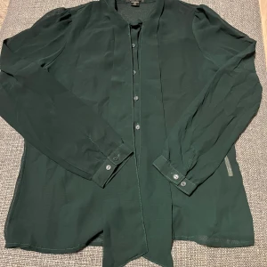 Mörkgrön blus från Amisu - Säljer en elegant mörkgrön blus från Amisu med långa ärmar och knappar framtill. Blusen har en lätt och luftig känsla, perfekt för att lyfta din outfit. 