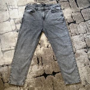 Grå jeans med rak passform - Säljer ett par grå jeans med klassisk femficksdesign och rak passform. Jeansen har normal midja, dragkedja och knapp framtill samt bälteshällor. Perfekta för en avslappnad stil. Helt nytt är nye använt så mycket