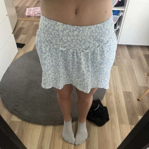 Ljusblå blommig kortkjol från Zara - Supersöt ljusblå kortkjol från Zara med vitt blommönster och volangdetalj upptill, kjolen har insydda shorts. Kjolen har en smockad midja som sitter bekvämt och ger en fin passform. Perfekt för vår och sommar! Priset går att diskuteras!!