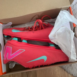 Röda Nike fotbollsskor med turkosa detaljer - Säljer ett par röda Nike fotbollsskor. Köptes i 17 april används 2-3 gånger Max köptes för 999