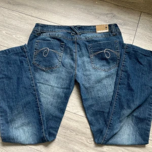 Jeans  - Säljer ett par klassiska blå jeans från Urban Heart med snygga kontrastsömmar och broderade bakfickor. Jeansen har normal passform och raka ben, perfekt för en avslappnad stil. Bälteshällor och knappstängning i midjan.