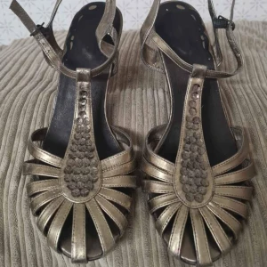 Guldiga sandaler med klack och öppen tå - Säljer ett par snygga vintage guldiga finskor med klack . Skorna har dekorativa detaljer framtill och rem runt vristen. Perfekta för dig som vill sticka ut lite extra!