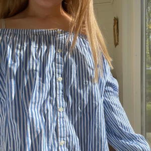 Offshoulder blus från Ralph Lauren - Säljer en jättegullig blå och vit randig offshoulder blus från Ralph Lauren. Vita knappar framtill. Blusen har stretchigt material upptill och vid handlederna. Perfekt för sommaren, är ganska liten i storleken❤️❤️