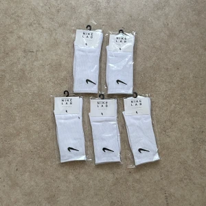 Vita Nike strumpor, 5 Pack - Säljer ett par klassiska vita Nike strumpor med svart broderad Nike-logga vid ankeln. Strumporna är ribbade och kommer i originalförpackning. Perfekta för dig som gillar sportig stil.