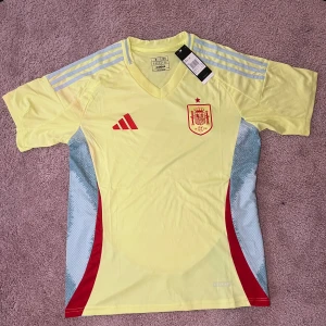 Spansk landslagströja i gult från Adidas - Säljer en gul fotbollströja från Adidas med Spaniens landslagsemblem på bröstet. Tröjan har röda detaljer, missfärgning vid armen som man kan se på sista bilden därav priset