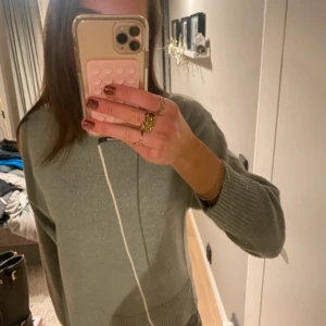 Ljusgrå stickad tröja - Säljer en ljusgrå stickad tröja med rund halsringning och långa ärmar. Tröjan har en klassisk och enkel design med ribbade muddar vid ärmslut och nederkant. Perfekt för lager-på-lager under kyliga dagar.