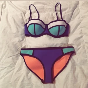Triangl Bikini - Säljer en cool bikini med färgblock i blått, mintgrönt och korall, markerade med svarta kanter. Överdelen har bygel och vadderade kupor, underdelen är klassisk trosa. Perfekt för stranden!