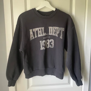 Mörkgrå sweatshirt  - Säljer en mörkgrå sweatshirt med trycket 'ATHL DEPT AMERICA 1983' framtill☺️