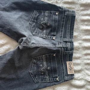Svarta jeans från Dolce & Gabbana - Säljer ett par svarta jeansbyxor från Dolce & Gabbana med snygga kontrastsömmar och broderade detaljer på bakfickorna. Klassisk femficksmodell med normal passform och låg midja. Storlek 36. Lite långa på mig (är 176cm) men man kan alltid klippa till sin längd 🩷
