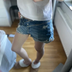 Blå jeansshorts med slitningar - Säljer ett par blå jeansshorts med slitna detaljer och rullade benslut. Som man ser på bilden är dom perfekta att vika ner ifall att man vill ha dom lågmidjade.😙