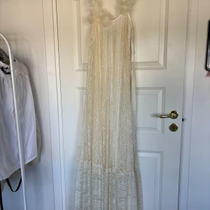 Vit spets- studentklänning från Ida Sjöstedt - Romantisk långklänning i vit spets från Ida Sjöstedt for Nelly. Klänningen har smala axelband dekorerade med stora blommor i organza och en vacker rosett i ryggen. Kan mötas upp! 