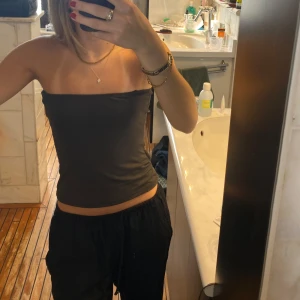 Mörkgrå tubtopp - Säljer en enkel och stilren mörkgrå tubtopp. Toppen är axelbandslös och har en tight passform som sitter snyggt mot kroppen. Perfekt att matcha med både jeans och kjol.