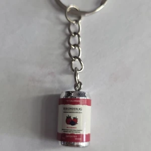 Nyckelring med Rekorderlig ciderburk - Säljer en unik nyckelring med en miniatyr av en Rekorderlig ciderburk som hänge. Perfekt accessoar för dig som gillar detaljer och vill ha något annorlunda på nyckelknippan. Burken har röd och vit design med jordgubbsdetalj.