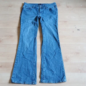 Blå bootcut jeans - Säljer ett par klassiska blå bootcut jeans med låg midja. Jeansen har fem fickor, bälteshällor och stängs med dragkedja och knapp. Perfekta för dig som gillar en retro vibe och vill ha ett par jeans med utsvängda ben.