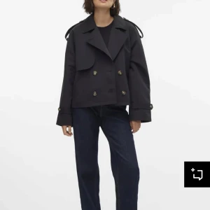 Svart kort trenchcoat  - Stilren svart kort trenchcoat från Filippa K med dubbelknäppning och klassisk krage. Jackan har axelremmar, knappar vid ärmslut och en snygg detalj baktill. Perfekt för dig som gillar minimalistisk och tidlös stil.