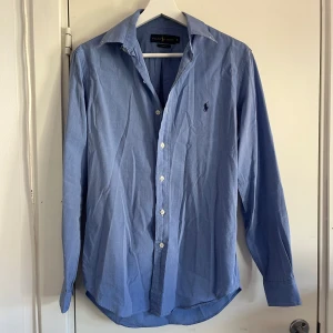 Ljusblå skjorta från Ralph Lauren - Jättefin ljusblå skjorta från Ralph Lauren i slim fit-modell. Jag har använt skjortan max 2 gånger så den är inprincip helt ny! Perfekt för en stilren och snygg look. Priset är inte hugget i sten. Vid mer frågor är det bara att höra av sig!