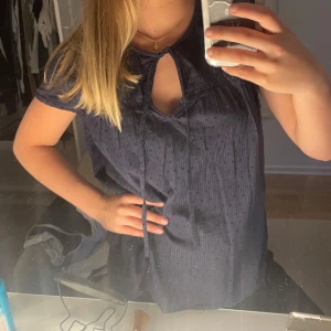 Mörkblå blus från Esprit - Mörkblå blus från Esprit med korta ärmar och knytband vid halsen. Blusen har diskreta ränder och spetsdetaljer över bröstet. Luftig och skön modell som passar perfekt till många tillfällen.