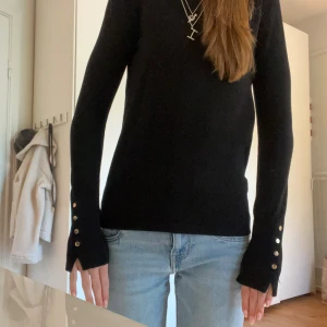 Svart tröja från Zara med knappar - Säljer en stilren svart tröja från Zara med långa ärmar och dekorativa knappar vid ärmsluten. Perfekt för en elegant look. Tröjan är i en mjuk och bekväm kvalitet. Finstickad, storlek S