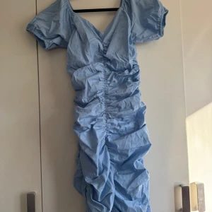 Ljusblå klänning från Gina Tricot - Säljer en ljusblå klänning från Gina Tricot med korta ärmar och en v-ringad design. Klänningen har en snygg rynkad detalj längs hela klänningen som ger en unik look. Perfekt för sommarens alla tillfällen! 💙 