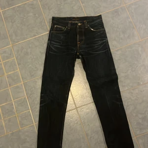 Nudie jeans - Snygga svarta jeansbyxor med klassisk femficksdesign och kontrasterande sömmar. Perfekta för en stilren look. De har en knapp och dragkedja framtil