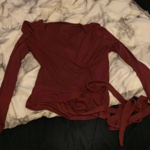 Vinröd omlottopp - Snygg vinröd omlottopp med långa ärmar och knytband i midjan. Perfekt för en stilren look. Köpte den men den passade inte mig, annars helt oanvänd