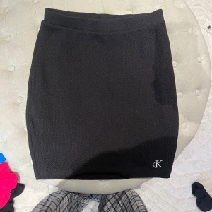 Svart kjol från Calvin Klein - Snygg svart kjol från Calvin Klein med en stilren design. Kjolen har en diskret logga i nederkant och är perfekt för en chic look. Tillverkad i ett bekvämt material som ger en bra passform.