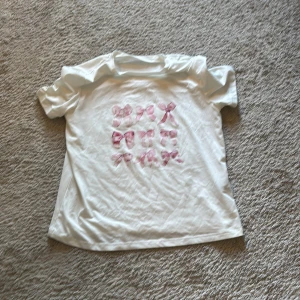 Vit t-shirt med rosa rosetter - Säljer en söt vit t-shirt med rosa rosetter på framsidan. Skriv om några frågor 💓
