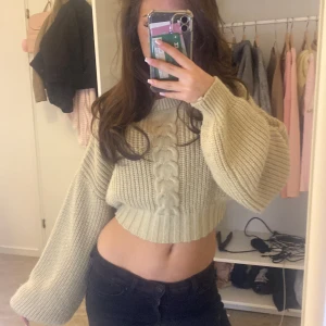 Beige stickad croppad tröja - Säljer en superfin beige stickad tröja med flätmönster framtill. Tröjan är croppad och har långa ärmar med ribbade muddar. Perfekt för en trendig look! 💫