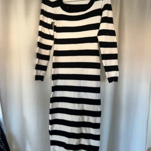 Randig långklänning i svart och vit - Snygg långklänning med breda svarta och vita ränder. Klänningen har långa ärmar och en rund halsringning. Perfekt för en stilren look.