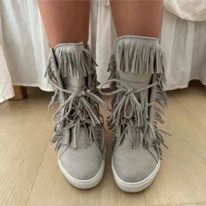 Grå mocka sneakers med fransar - Snygga grå sneakers i mocka med fransdetaljer och snörning. Perfekta för en unik stil med en touch av bohemisk känsla. Skorna har en rund tå och en bekväm sula.