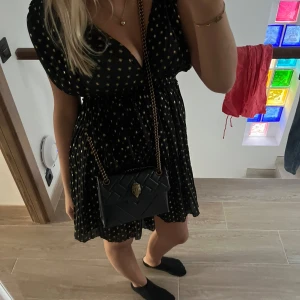 Svart kortklänning med guldprickar - Snygg svart kortklänning med guldprickar och v-ringning. Klänningen har korta ärmar och mer tajt i midjan för en smickrande passform. Perfekt för en kväll ute eller en speciell tillställning.