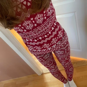 Röd och vit jultröja med snöflingor - Säljer en mysig röd och vit tröja och byxor med snöflingor och hjärtan, från Rusta. Tröjan och byxorna är tillverkad i polyester och elastan, vilket ger en skön stretch. Den har långa ärmar och ett klassiskt julmönster. 