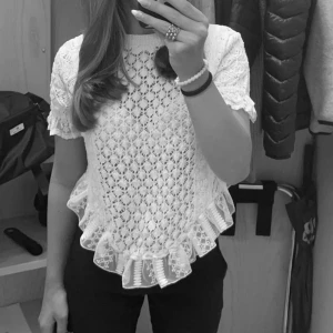 Vit spetsblus med volangdetaljer från Zara i str S - Säljer en söt vit spetsblus från Zara str S med korta ärmar och volangdetaljer vid nederkanten. Perfekt för en somrig look eller en speciell tillställning. Blusen har ett vackert mönster och ger en romantisk känsla.