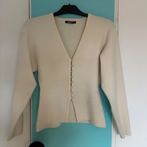 Vit kofta från Gina - Säljer en stilren vit kofta från Gina med v-ringning och knappar framtill. Koftan har långa ärmar och figursydd design. Tecken på användning förekommer. På sista bilden kan man se att tröjan är lite nopprig i ena hörnet! Annars i ett väldigt bra skick🩷