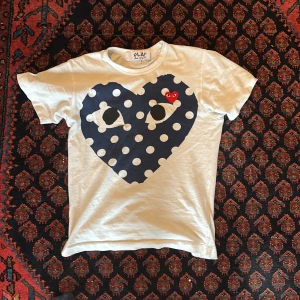 Vit t-shirt från Comme des Garçons - Säljer en vit t-shirt från Comme des Garçons med ett stort blått hjärta med vita prickar och ett rött broderat hjärta med ögon. Perfekt för dig som gillar unika och stilrena plagg!