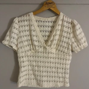 Vit blus med v-ringning - Säljer en söt vit blus med v-ringning och korta ärmar. Blusen har ett diskret mönster och är perfekt för både vardag och speciella tillfällen. Den är tillverkad i ett lätt och luftigt material.