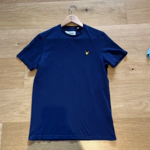 Mörkblå t-shirt från Lyle & Scott - Säljer en snygg mörkblå t-shirt från Lyle & Scott i ekologisk bomull. T-shirten har en liten gul broderad logga på bröstet och är kortärmad. Perfekt för en stilren och bekväm look. Storlek: XS