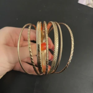 Guldarmband i set - Säljer ett set med flera guldarmband. Armbanden har olika texturer och mönster, vilket ger en snygg och varierad look. Perfekt för att stapla och skapa en unik stil.
