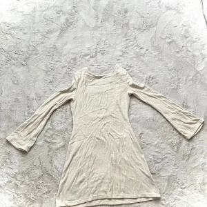 Beige ribbad klänning - Säljer en stilren beige klänning med ribbad struktur. Klänningen har långa ärmar och en enkel design som passar perfekt för olika tillfällen. Perfekt för dig som gillar en minimalistisk stil. Öppen i rygg