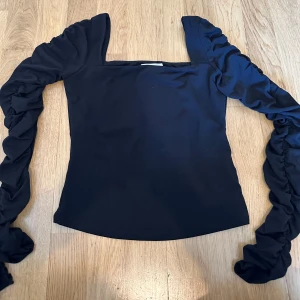 Svart långärmad topp med rynkade ärmar - Snygg svart topp med långa ärmar och fyrkantig halsringning. 