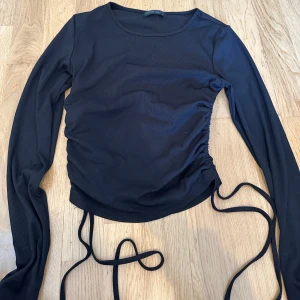 Svart topp med snörning - Snygg svart rtopp med långa ärmar och snörning i sidan för en justerbar passform. 