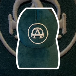 Mörk grön keps med broderad logotyp - Snygg grön keps från All Cap One med en broderad vit logotyp framtill. Kepsen har ett nätmaterial baktill för bättre ventilation och en justerbar passform. Perfekt för en avslappnad stil.