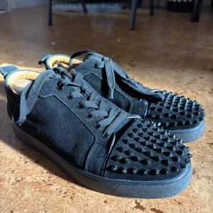  Christian Louboutin skor - Säljer ett par svarta sneakers i mocka från Christian Louboutin med svarta nitar. Ingen box med följer