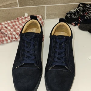 Mörkblåa skor från Louboutin  - Säljer ett par mörkblå sneakers från Christian Louboutin med ovandel i mocka och klassisk röd sula undertill. Den enda skadan är snöret men det syns nästan inte 9/10 skick orginal pris 6500